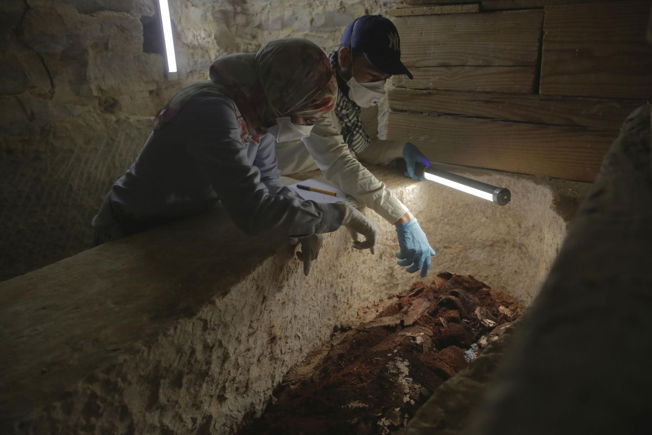 Two archaeologists, Maysa Rabeeh (L) and Mohammed Refaat (R) examine the degraded wooden coffin of Ayawet with a light wand. They are inspecting the remains for evidence of a second burial. [credit: foto di Piers Leigh; Copyright National Geographic]